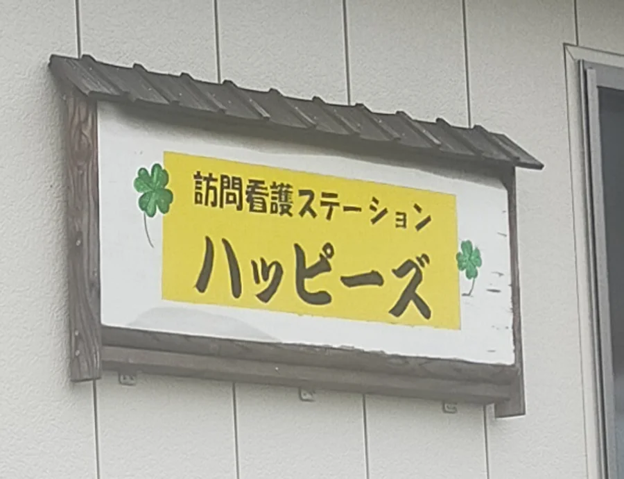 木の屋根がついた看板。黄色い地に「訪問看護ステーション ハッピーズ」とクローバー